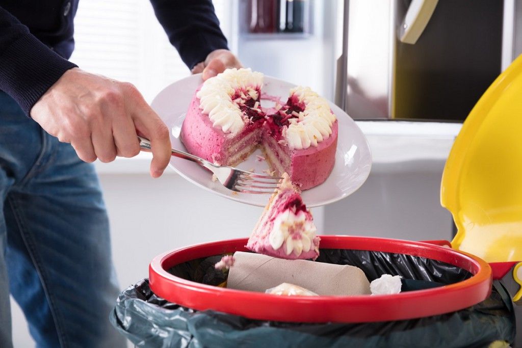 92388745 - close-up of a human hand throwing cake in trash bin