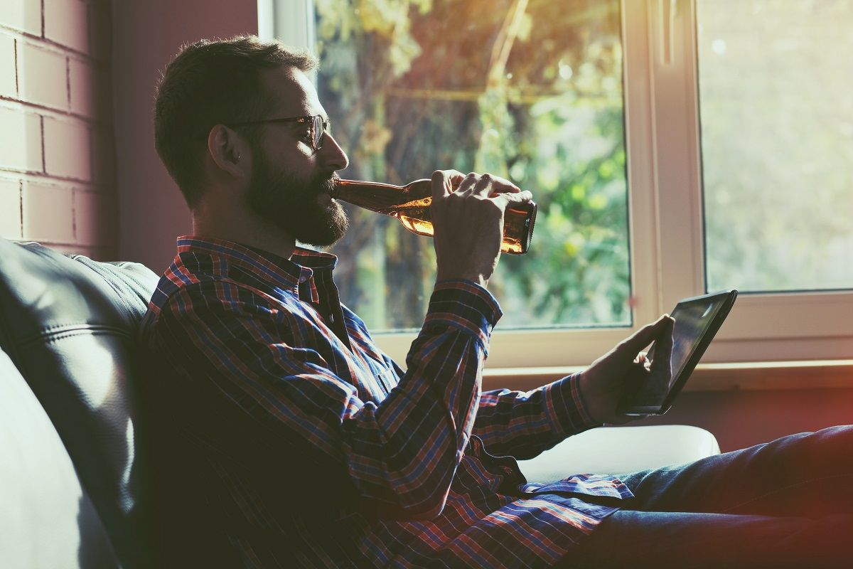 bearded man with digital tablet pc drinking bottle of beer
