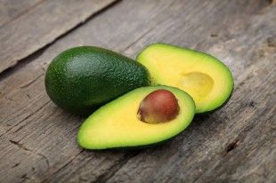 55867734 – two avocados one cut in two with seed, on wooden surface