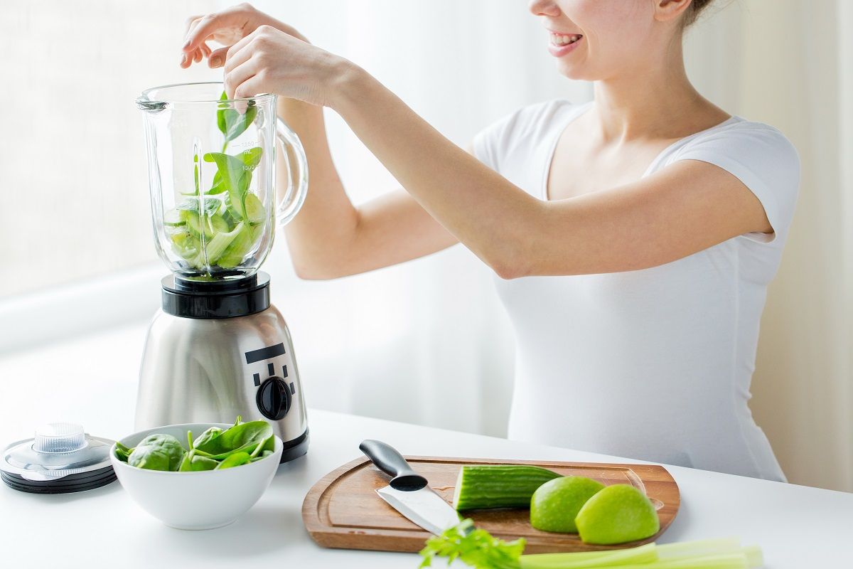 close up of woman with blender and vegetables