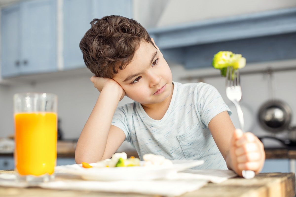 Sad boy looking at the green vegetable on his fork