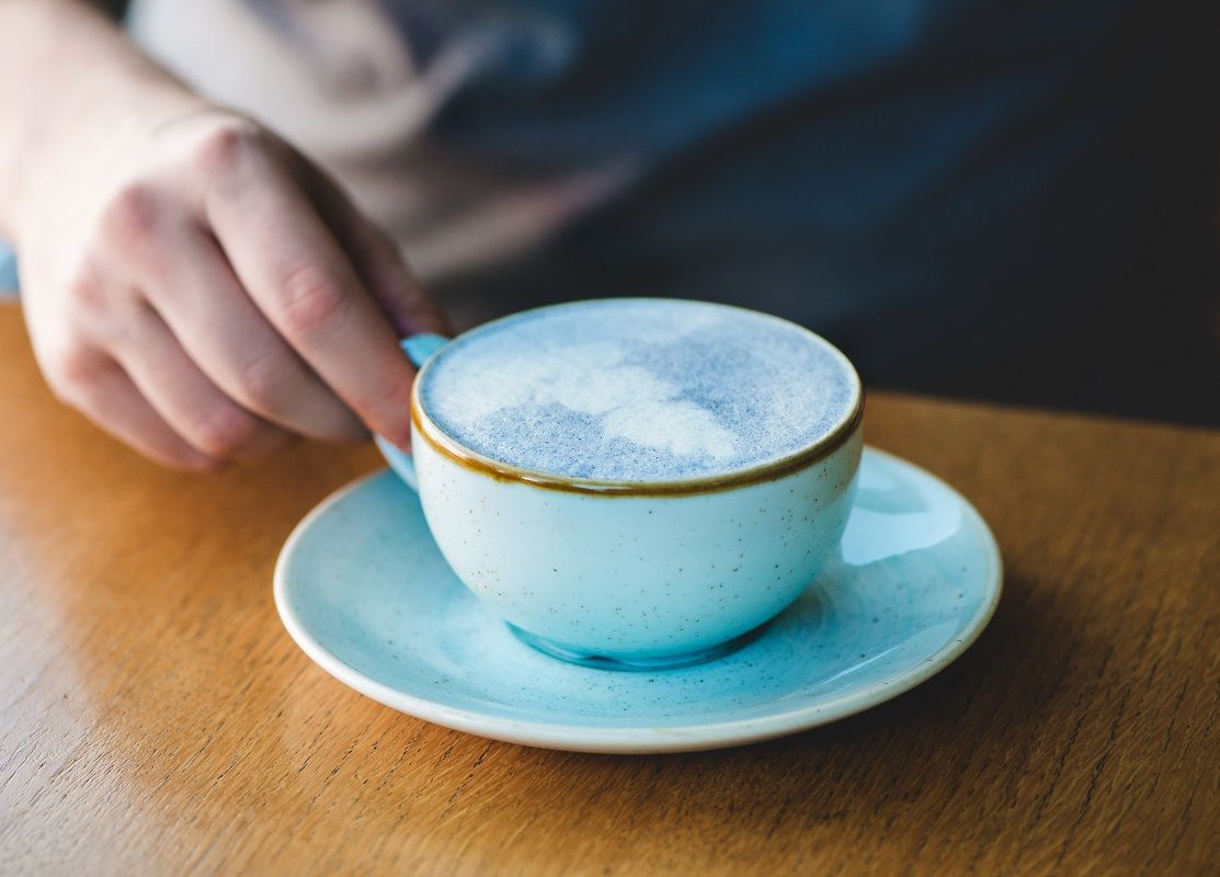 Man holding blue matcha tea latte in cafe.