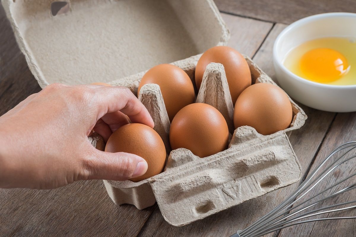 Woman hand selected egg in egg carton and yolk in bowl