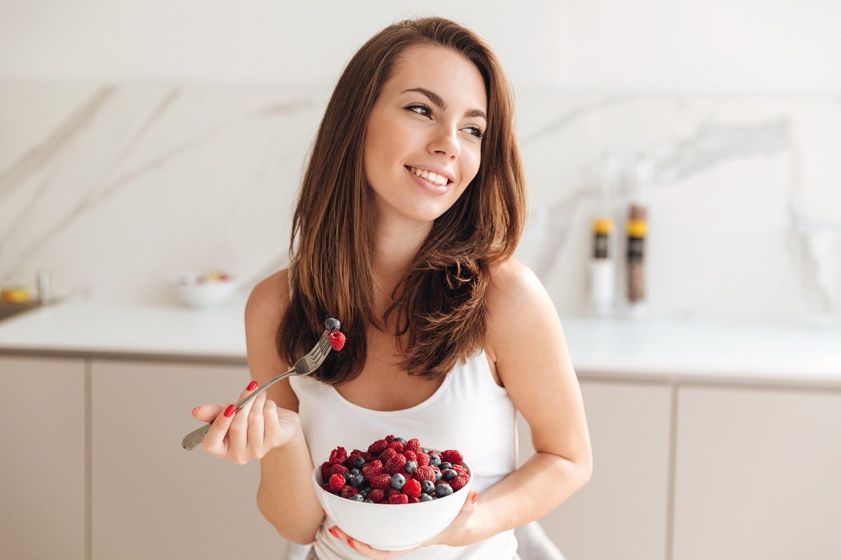 Happy young woman holding bowl with fresh berries