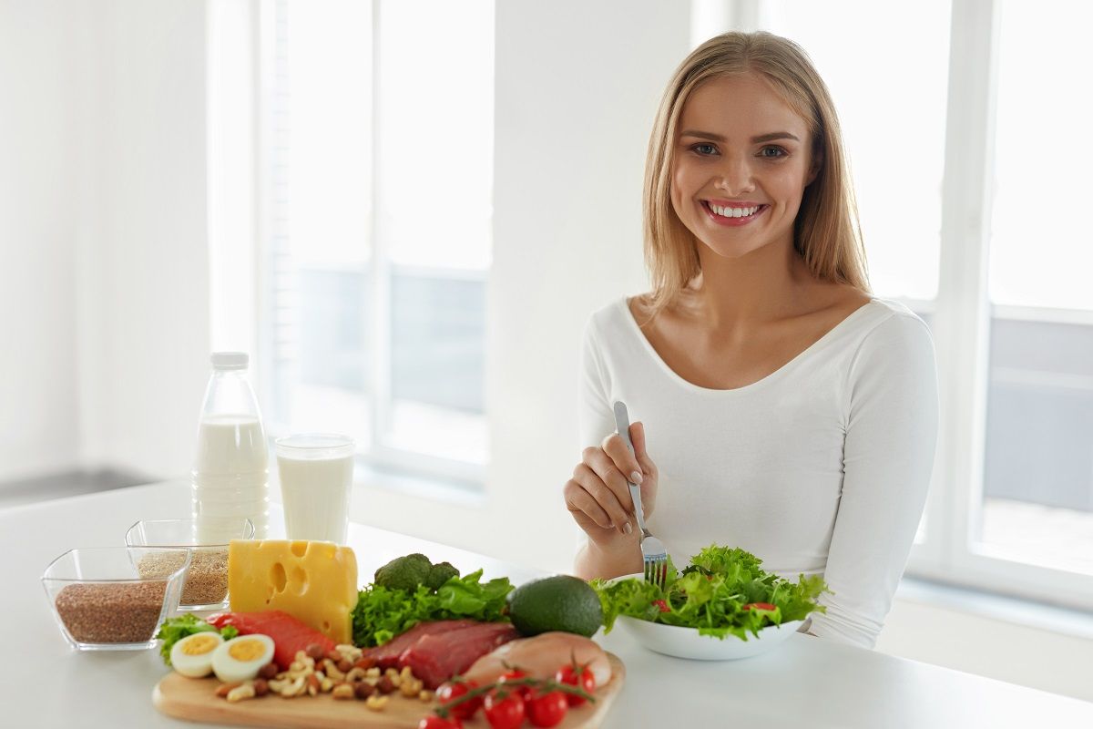 Beautiful Woman With Salad And Food Products On Table In Kitchen