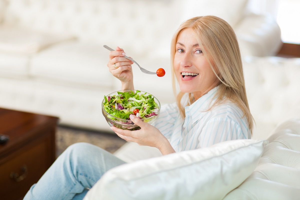 Mature woman sitting on a couch at home while eating a salad