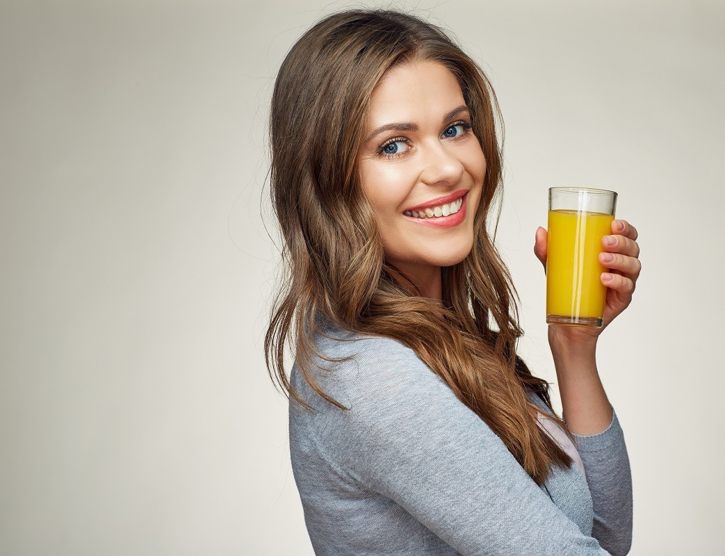 woman holding glass with orange juice smiling with teeth.