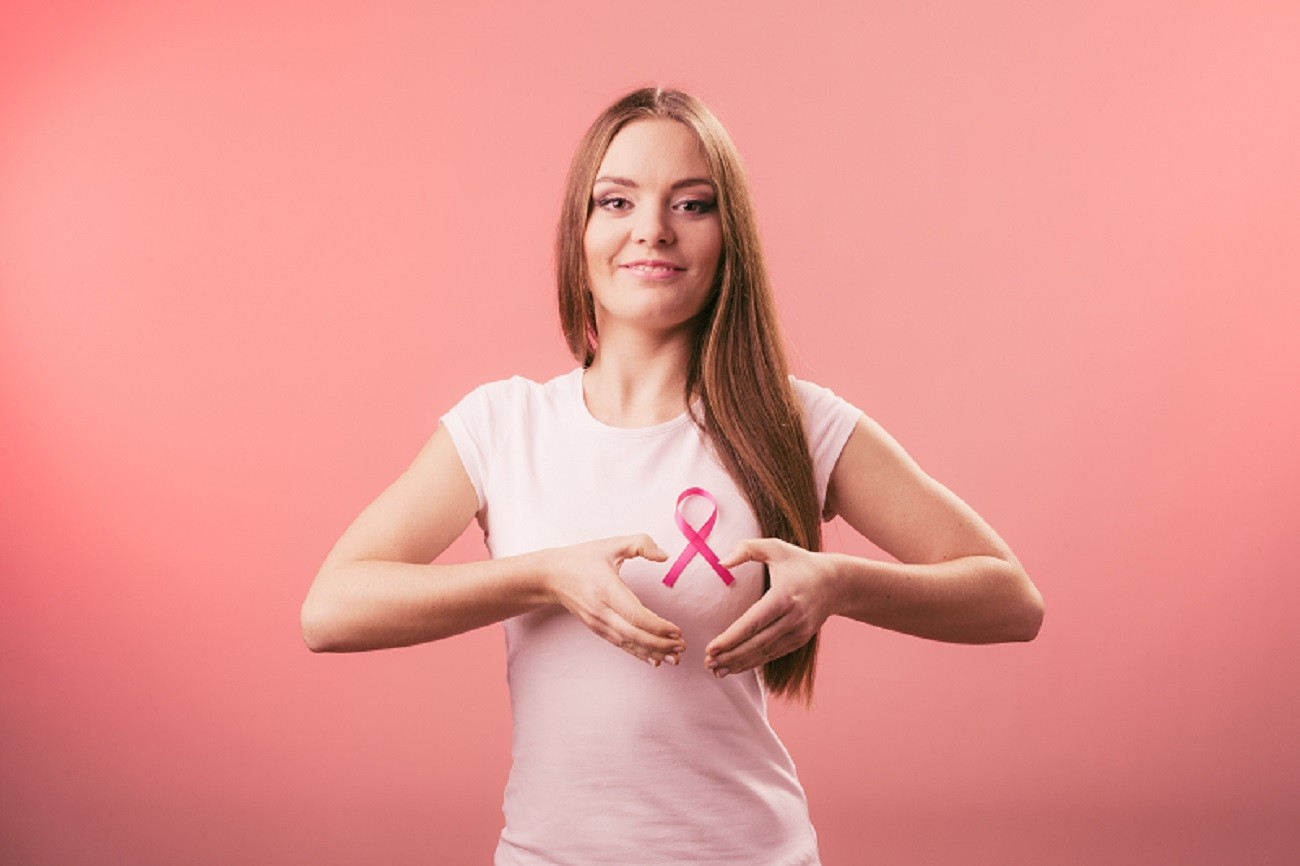Breast cancer. Woman making heart shape on pink ribbon
