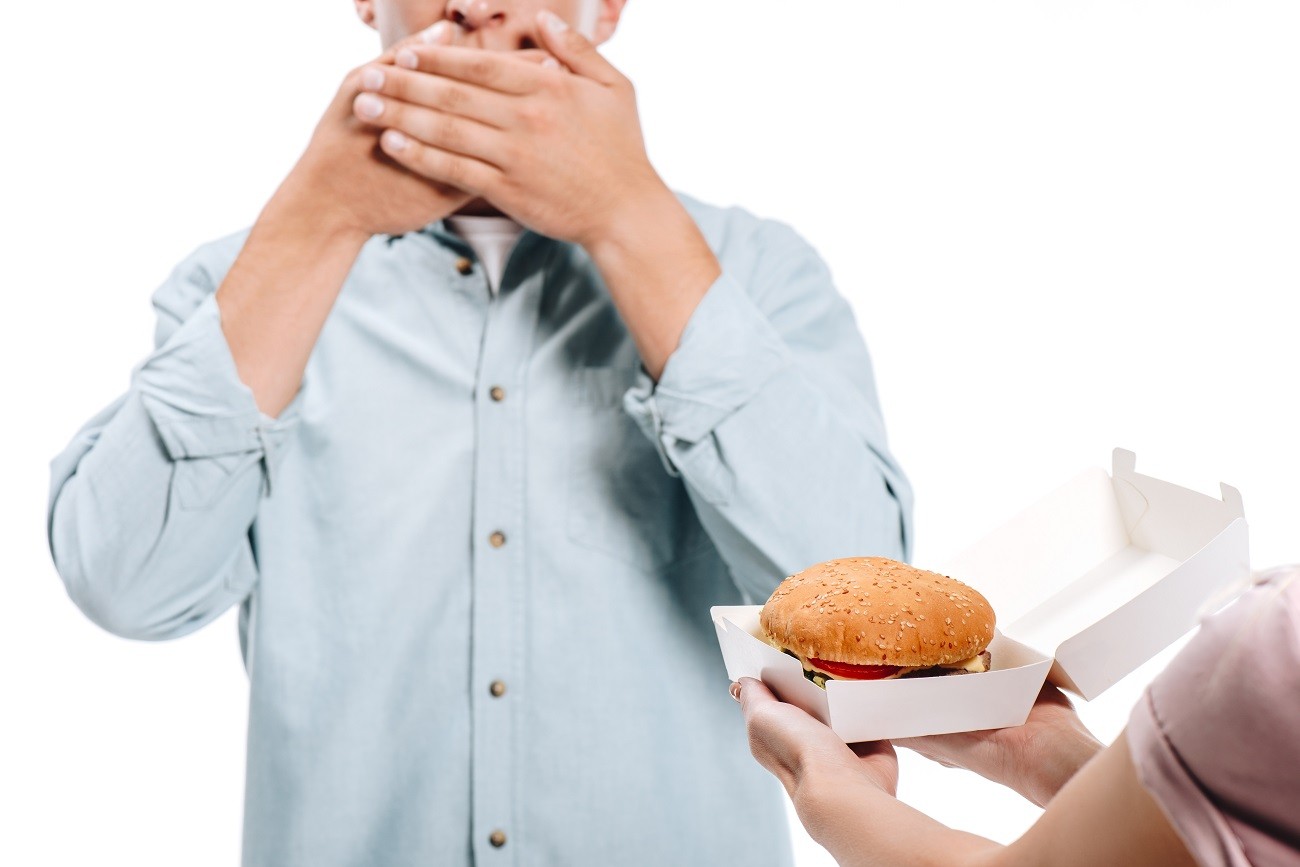 cropped image of man covering mouth, woman proposing burger isolated on white