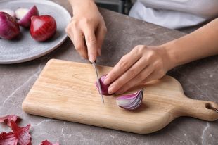 Woman cutting ripe red onion on table
