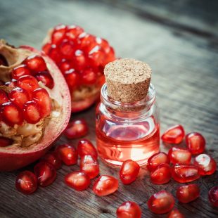 Pomegranate oil in bottle and open garnet fruit with seeds on wo