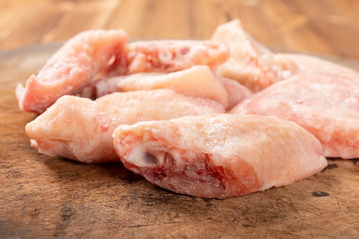 side view frozen raw chicken wings on chop board