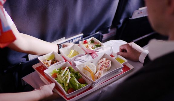 Midsection of stewardess holding tray with airplane food on blue background. Stewardess brought lunch, businessman, first class, high level of service on the plane