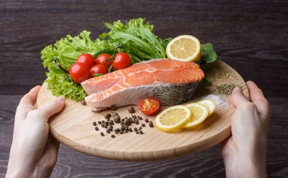 Woman holding a wooden plank with raw salmon