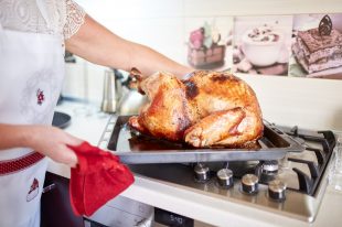 Woman taking turkey out of oven on a kitchen background. Roasted, traditional turkey cooking. Christmas turkey.