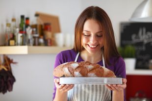 Young woman holding tasty fresh bread in her kitchen