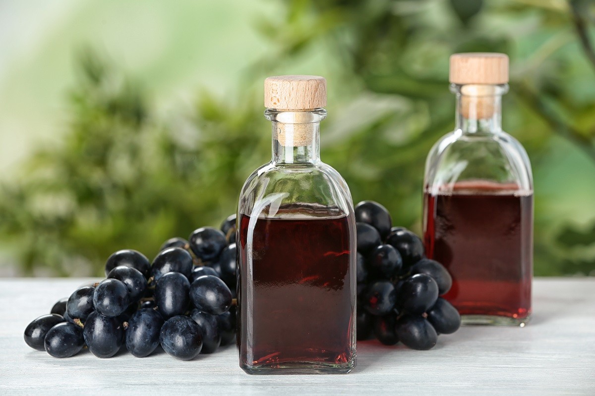 Bottles with wine vinegar and fresh grapes on wooden table against blurred background
