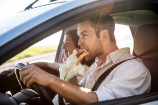 22108599 – couple in car – man is driving and eating baguette