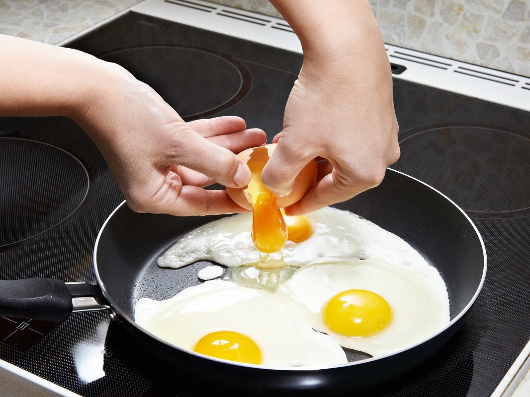 36928987 – woman breaks an egg in fried eggs close up