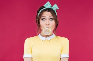 Amazed cute pinup girl blowing a bubble gum balloon