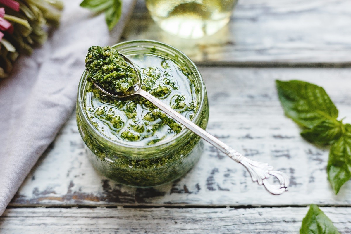 Pesto sauce in vintage spoon on glass jar of pesto sauce with ingredients,fettuccine on rustic white wooden table. Traditional Italian pesto recipe for making pasta, spaghetti, bruschetta,pizza.