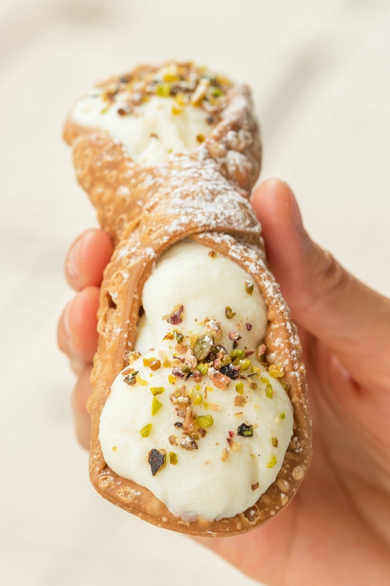 Close up of a fresh Sicilian Cannoli, held by hand. .