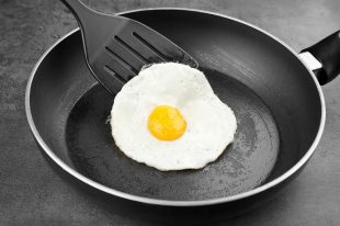Homemade over easy egg with spatula in frying pan on dark background