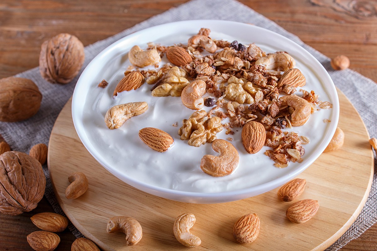 White plate with greek yogurt, granola, almond, cashew, walnuts