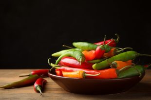 Hot chili peppers in plate on wooden table against black background