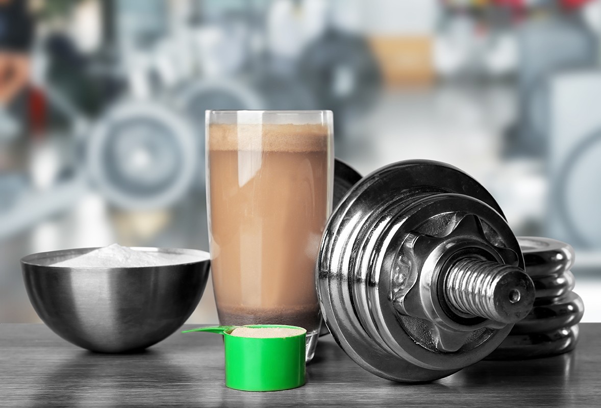 Glass of protein shake and dumbbell on table in gum