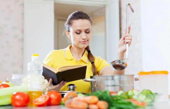 21503857 – woman cooking   food with book at  kitchen