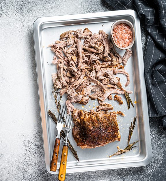 Texas bbq smoked puilled pork meat in a steel baking tray. White background. Top view. Copy space