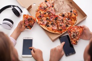 Young teenagers checking their phones while eating pizza – top v