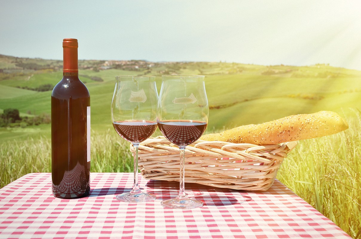 Red wine and bread on the chequered cloth against Tuscan landscape. Italy