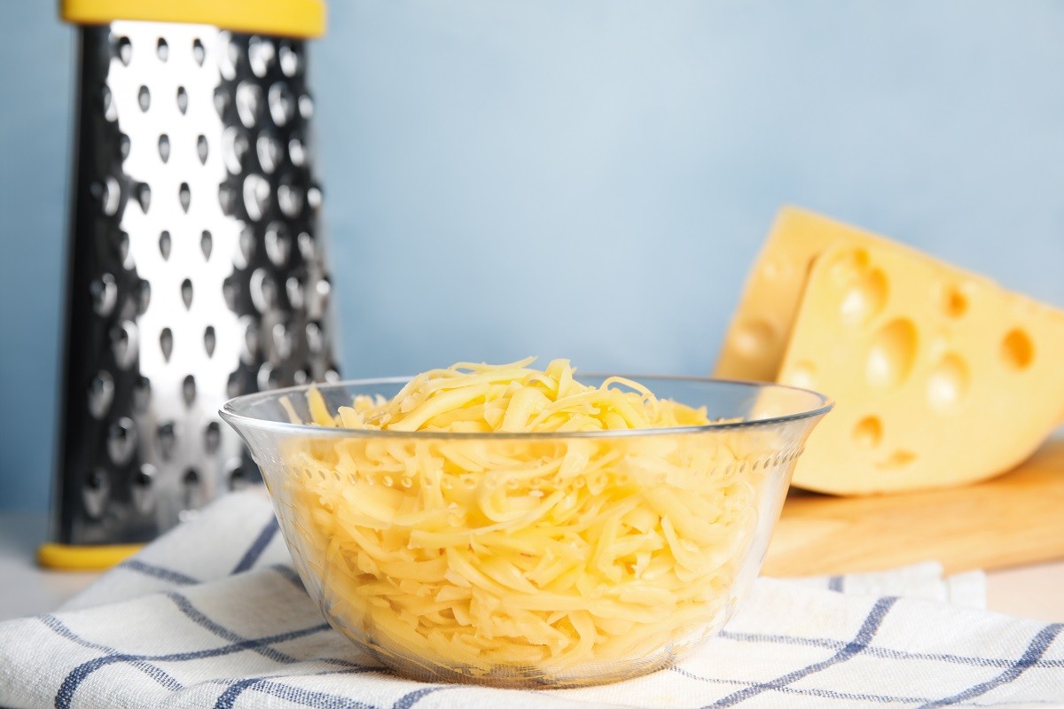 Delicious grated cheese in glass bowl on table