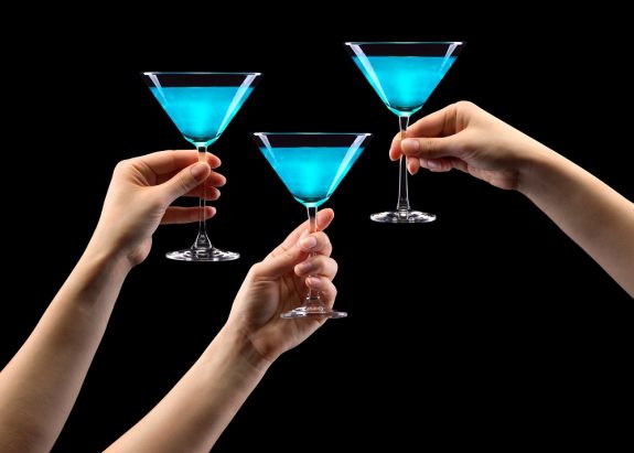 Set of hands holding blue martini glass isolated on black.