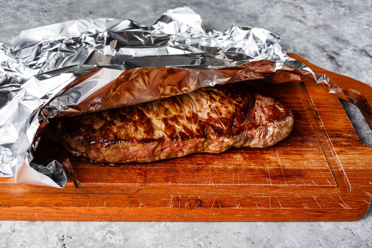Grilled,Steak,Resting,On,Wooden,Board,Covered,With,Aluminum,Foil