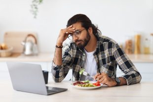 Exhausted middle-eastern man freelancer having snack while working from home