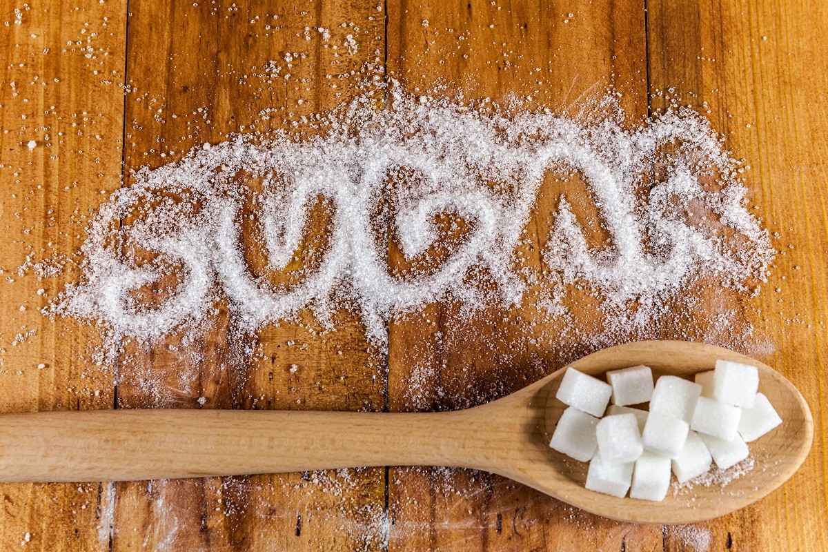 The word sugar written into a pile of white granulated sugar with spoon of sugar cubes over wooden background