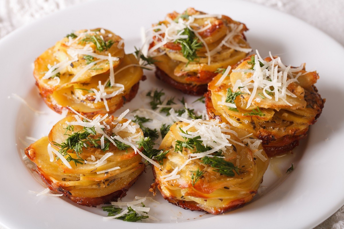 Baked sliced potatoes with cheese and dill close-up on a plate.