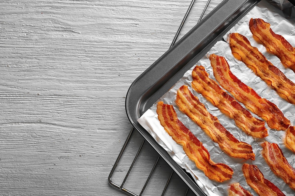 Baking tray with strips of fried bacon on  wooden table