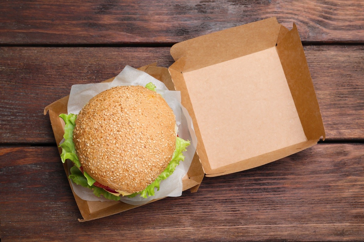Delicious burger in cardboard box on wooden table, top view