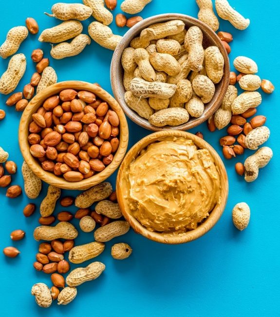 Make peanut butter with nuts and paste in bowl on blue background top view copyspace