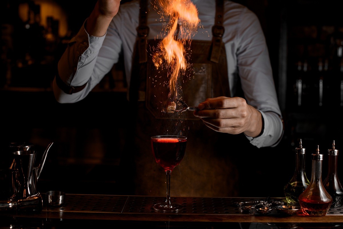 Bartender holds fired up sugar above alcohol cocktail