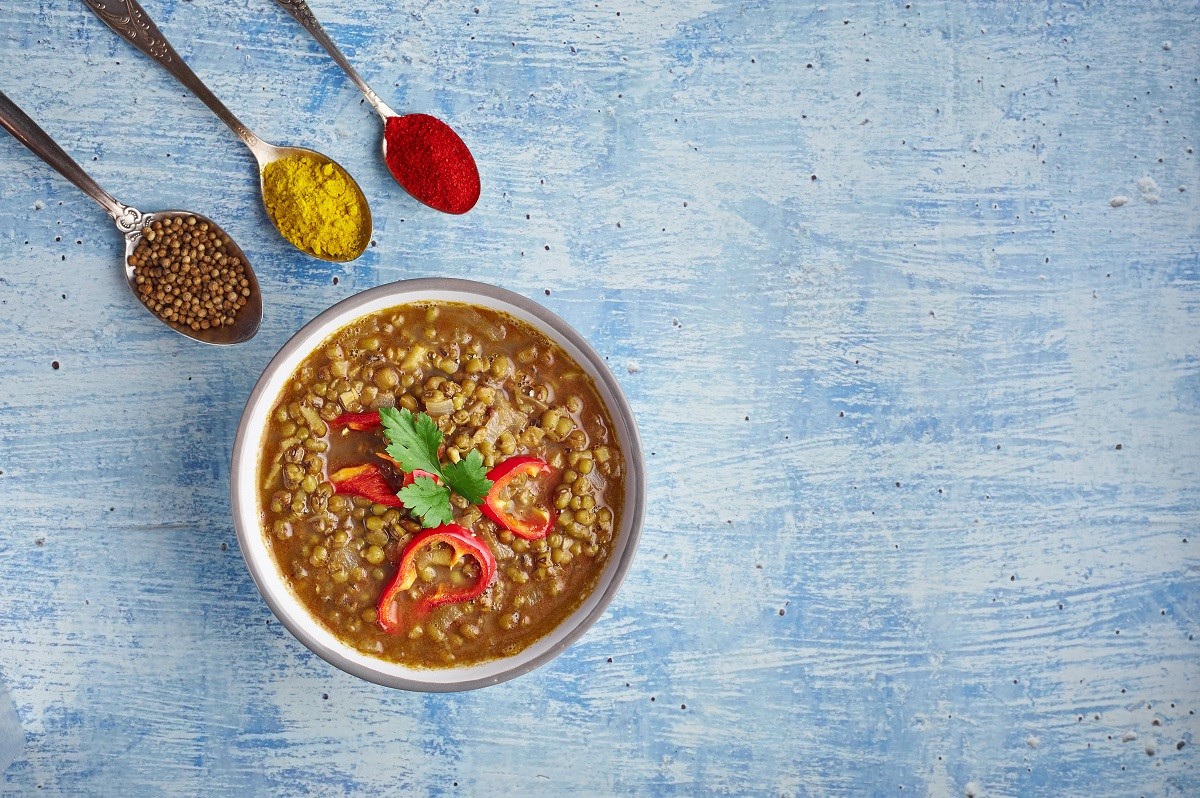 Mung Dhal decorated with red pepper slices at blue tabletop. Moong Dal – Indian Cuisine curry.