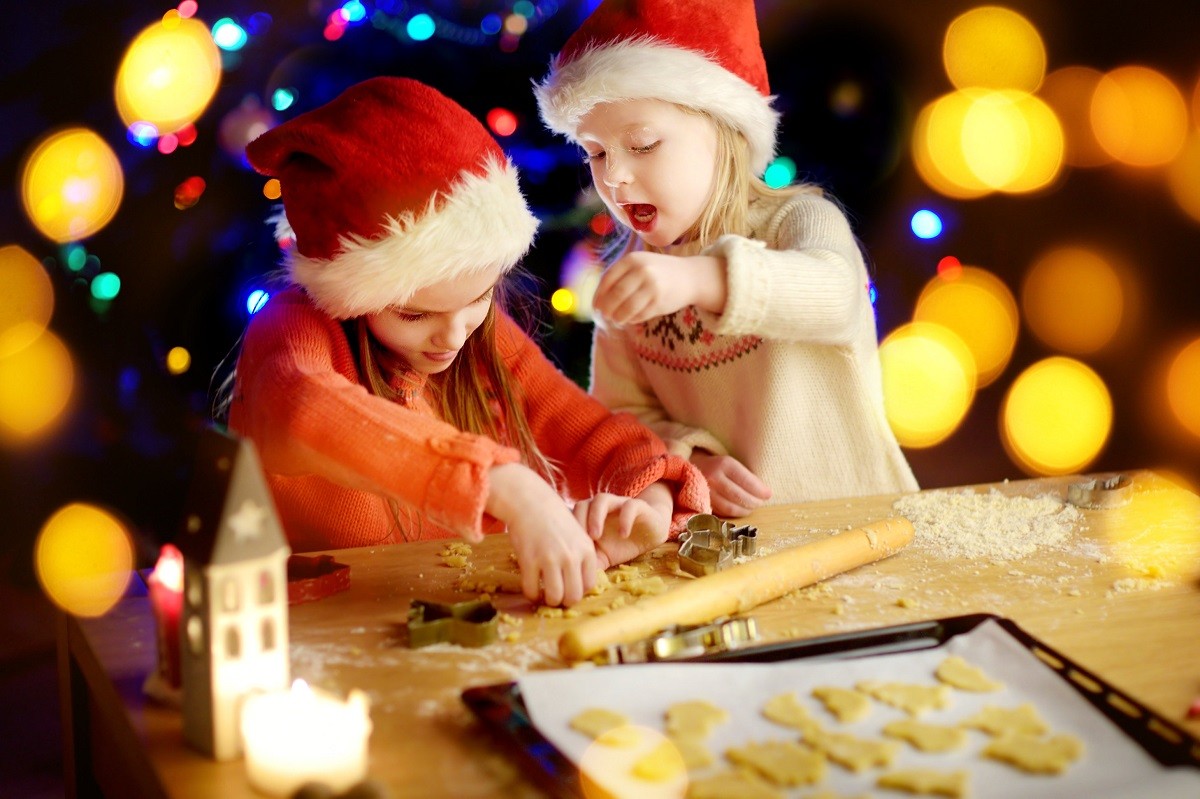 Two adorable little sisters baking Christmas cookies by a fireplace