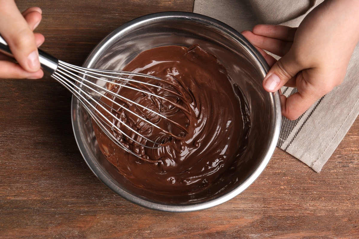Woman stirring delicious chocolate sauce in bowl with whisk on table