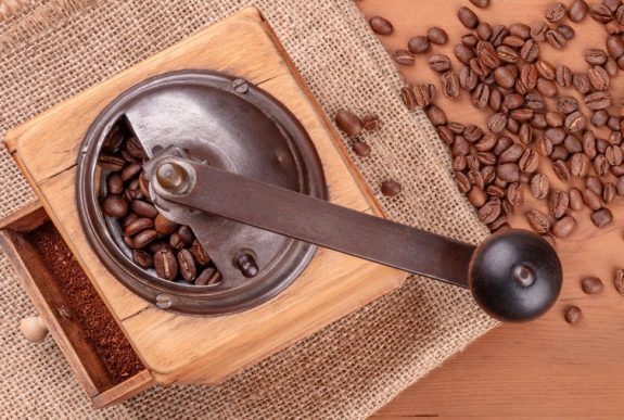 An overhead photo of a vintage coffee grinder with roasted coffee beans, shot from the top on a rustic background with copy space