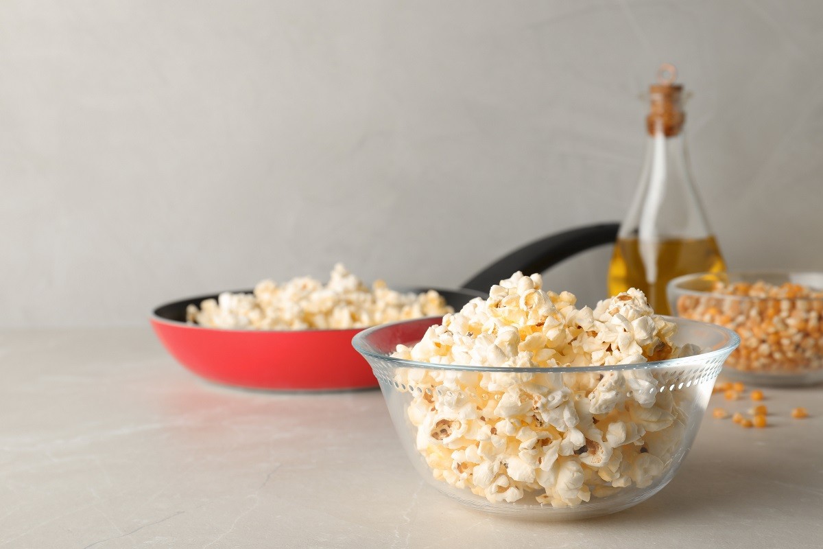 Glass bowl with tasty popcorn on grey table. Space for text