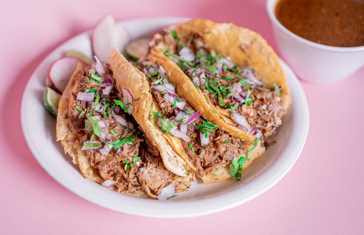 Delicious tacos of birria on a white plate with a broth in the back.